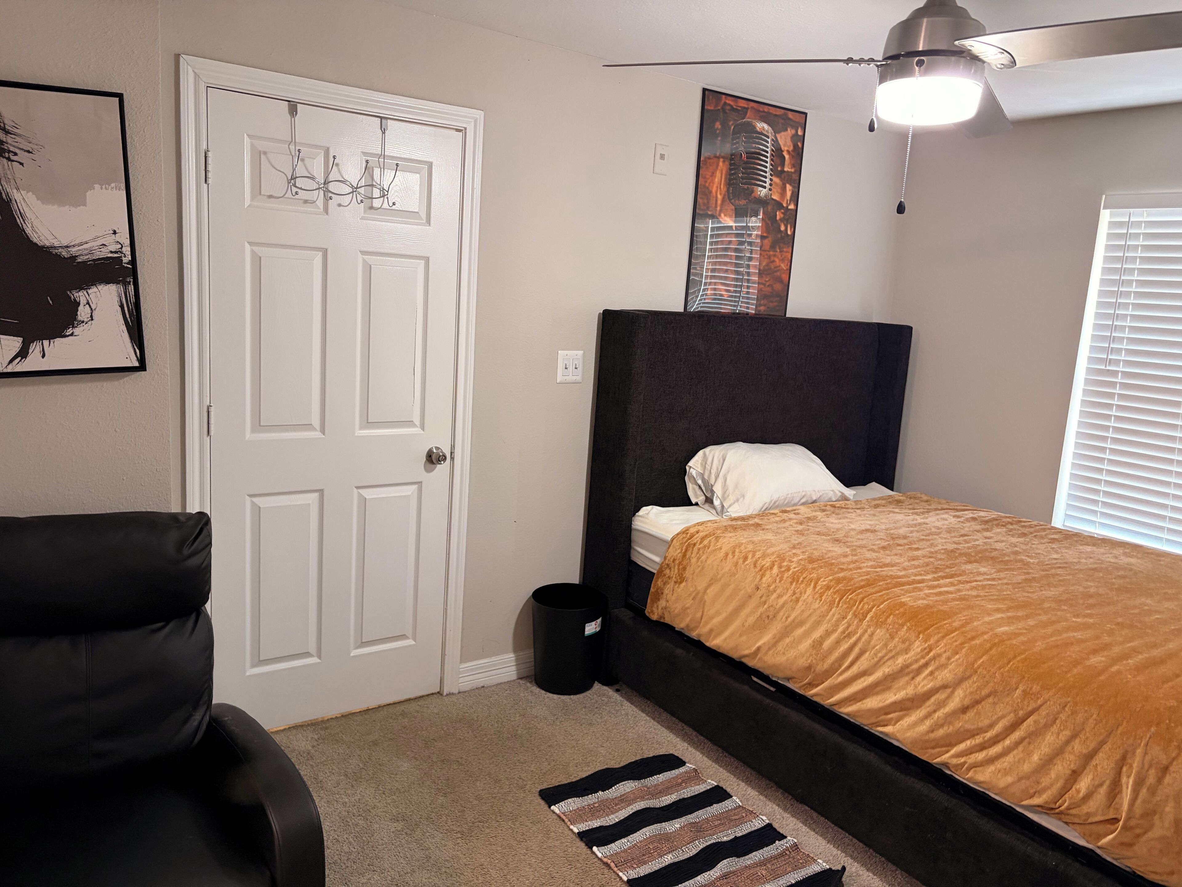 A bedroom with a bed, a chair, a door, and a ceiling fan.