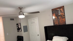 Een slaapkamer met een bed, een plafondventilator, een deur, een stoel en een poster aan de muur.