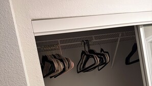 Een kast met hangende kleding en een plank.