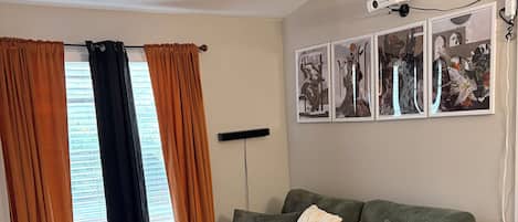 Una sala de estar con un sofá verde, un tapete rojo y naranja, un ventilador de techo y un proyector en la pared.