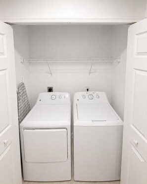 A laundry room with two white front-loading washing machines, a metal drying rack, and a towel rack. - Charming Vero Beach Home with Tesla Charger and Office Space (Vero Beach)