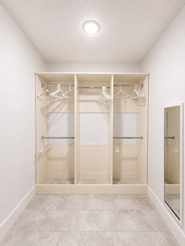 A walk-in closet with multiple shelves and hanging space, a mirror, and a tiled floor.