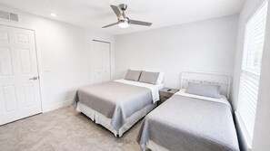 A bedroom with two beds, a ceiling fan, and a window with blinds.