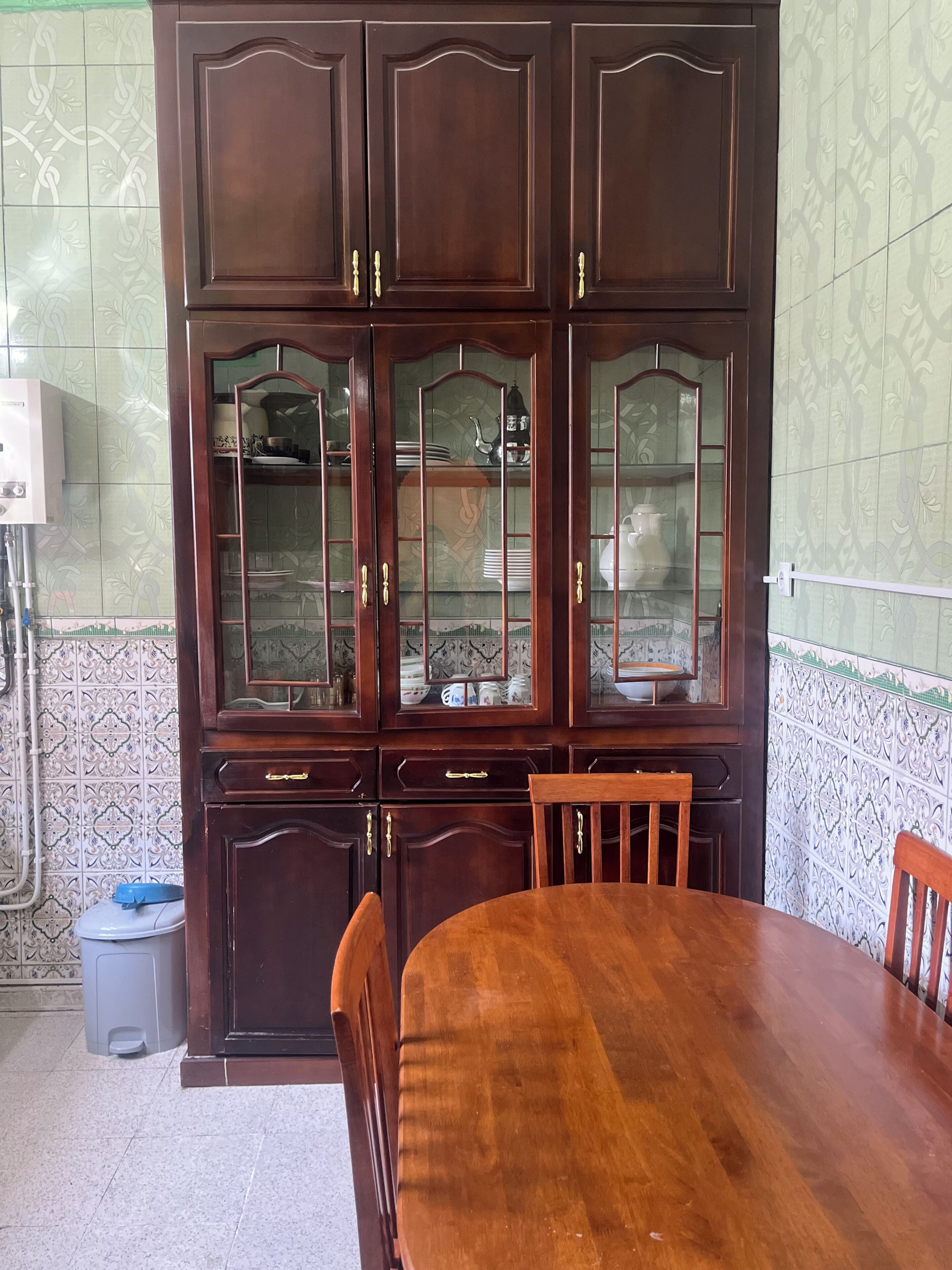 Een eetgedeelte met een houten tafel en stoelen, een kast met glazen deuren en betegelde muren.