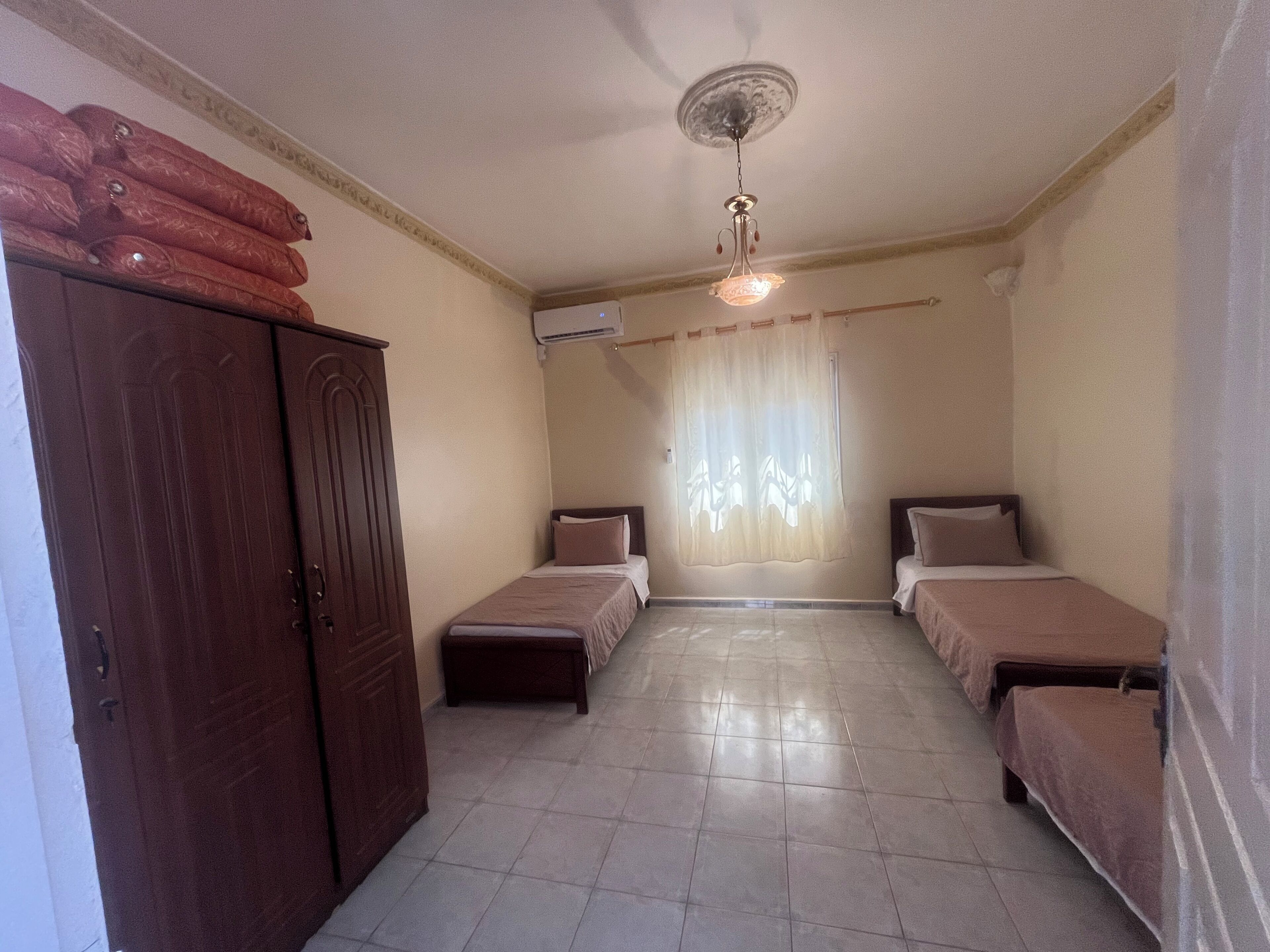 A room with two beds, a wardrobe, a ceiling fan, and a window with curtains.