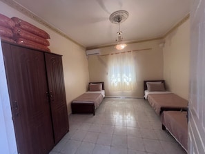 A room with two beds, a wardrobe, a ceiling fan, and a window with curtains. - Family Apartment in Aïn El Turk – 7-minute walk to the beach (Ain turk)
