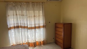 Una stanza con un letto, una cassettiera e una finestra con tende leggere.
