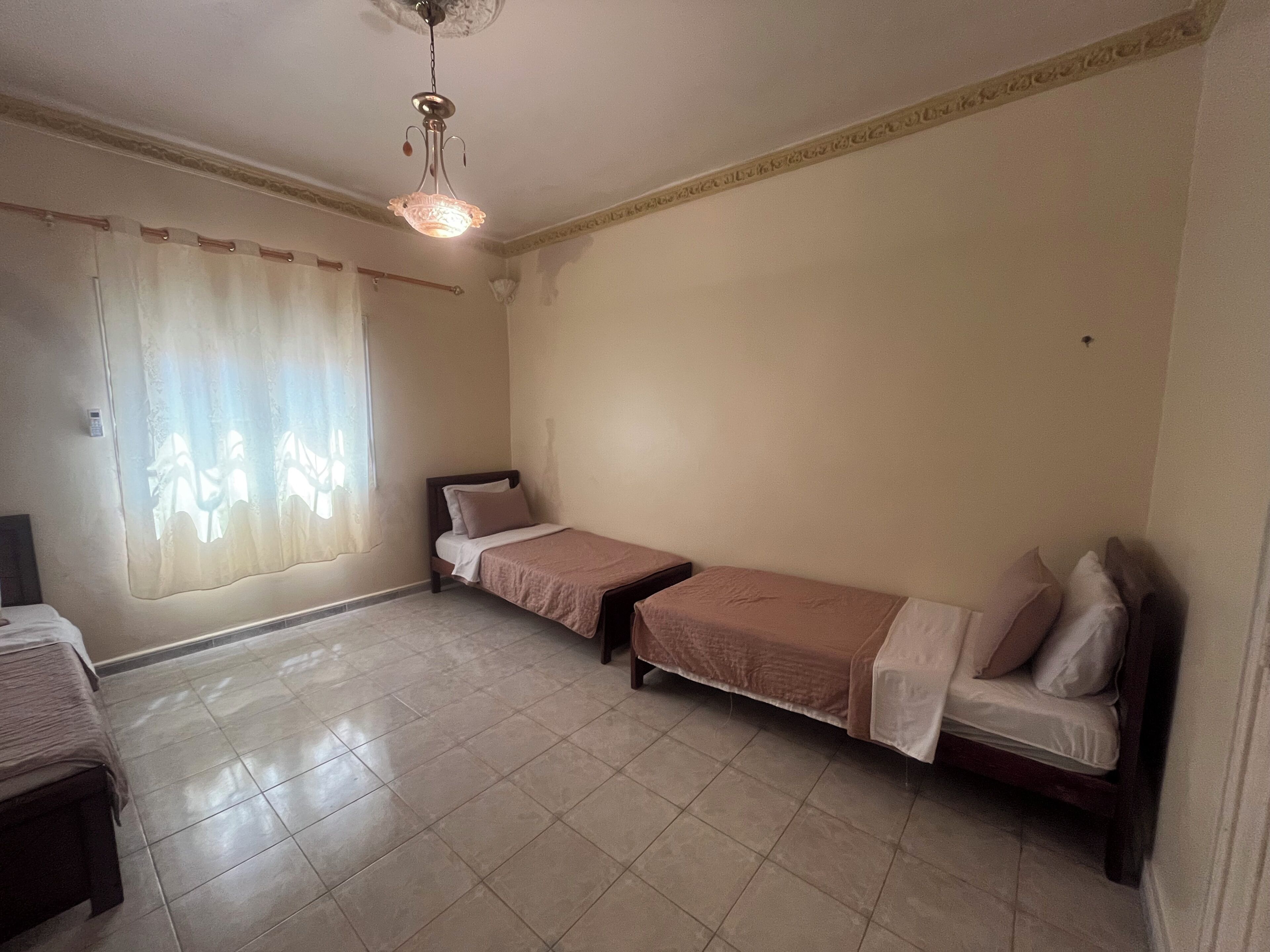Une chambre avec deux lits simples, un ventilateur de plafond et une fenêtre avec des rideaux.