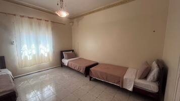 Une chambre avec deux lits simples, un ventilateur de plafond et une fenêtre avec des rideaux.