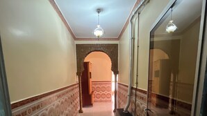 Un corridoio con pareti decorate, pavimento piastrellato, una luce a soffitto e una porta che dà su un'altra stanza.