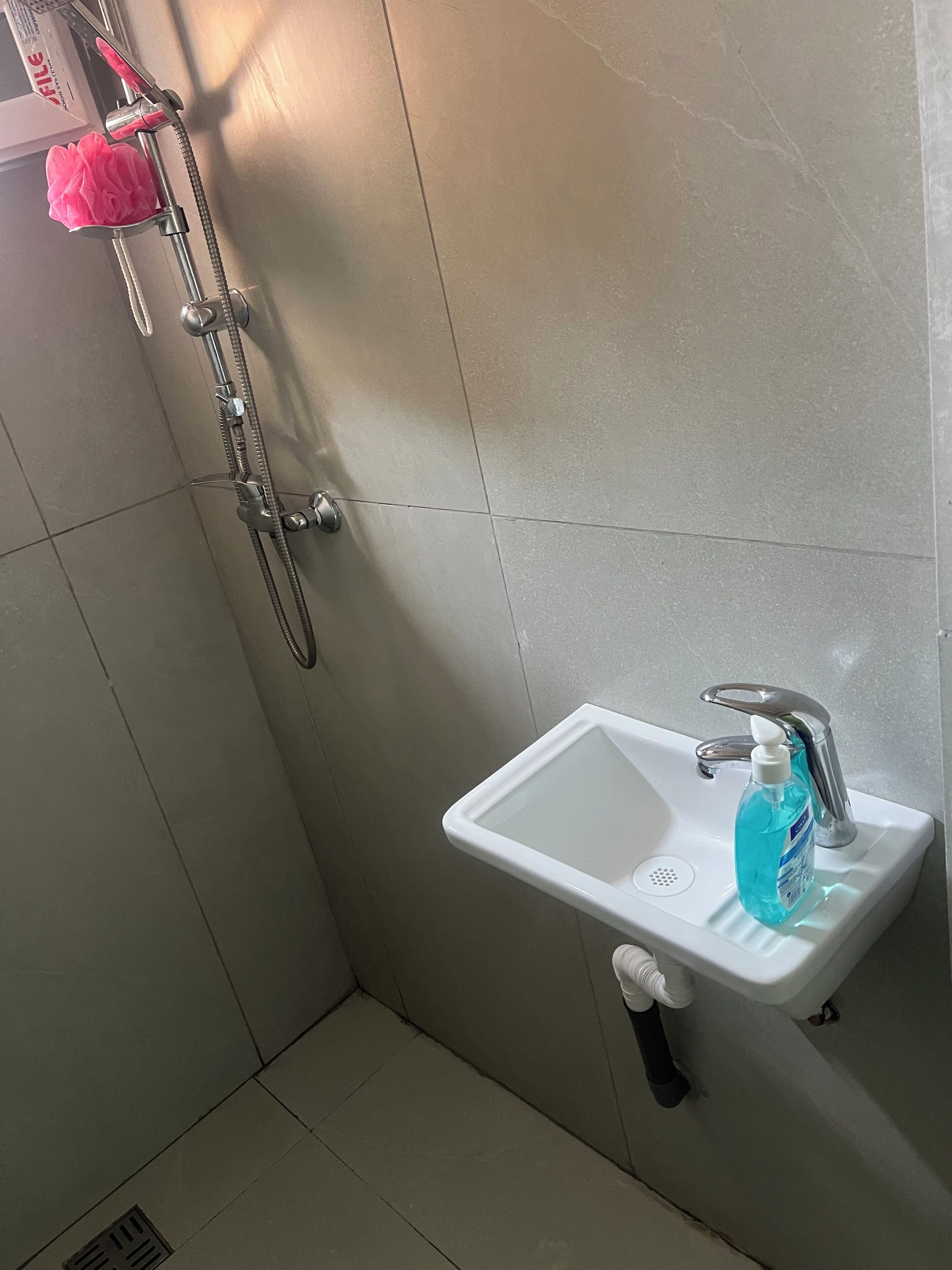 Une salle de bain avec une douche, un lavabo et une bouteille de liquide bleu.
