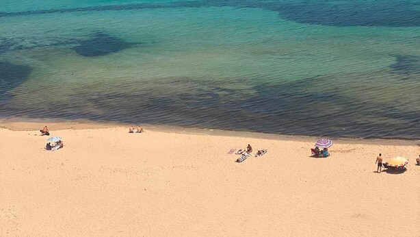 Una spiaggia con acque turchesi cristalline, una riva sabbiosa e un promontorio roccioso all'orizzonte.