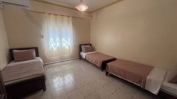 Een kamer met twee bedden, een raam met gordijnen, een plafondlamp en een airconditioning.