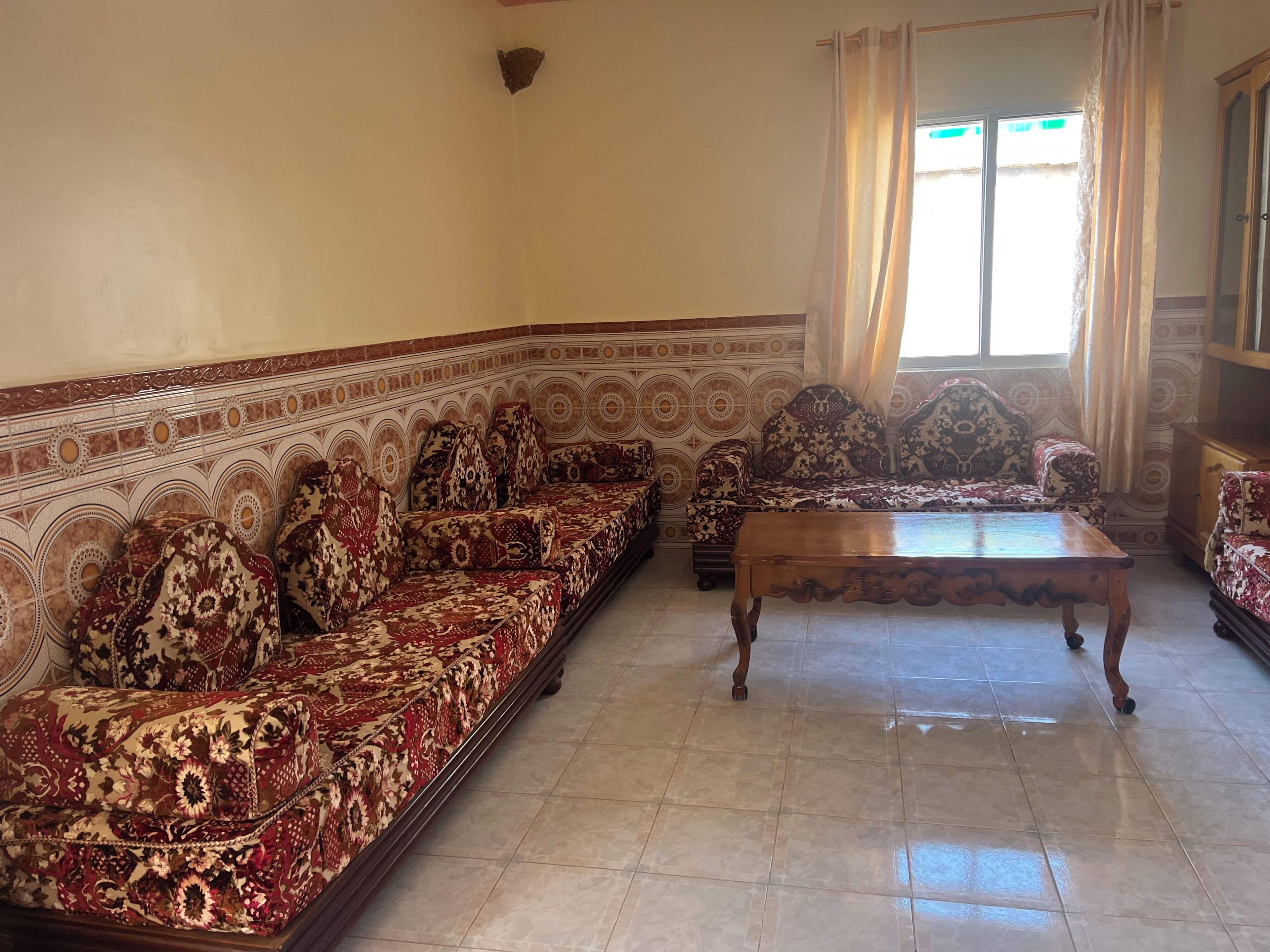 Una sala de estar con un sofá estampado, una mesa de centro de madera y una ventana con cortinas.