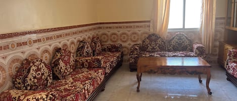A living room with a patterned sofa set, a wooden coffee table, and a window with curtains.