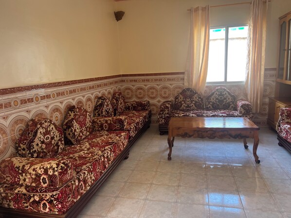 A living room with a patterned sofa set, a wooden coffee table, and a window with curtains.