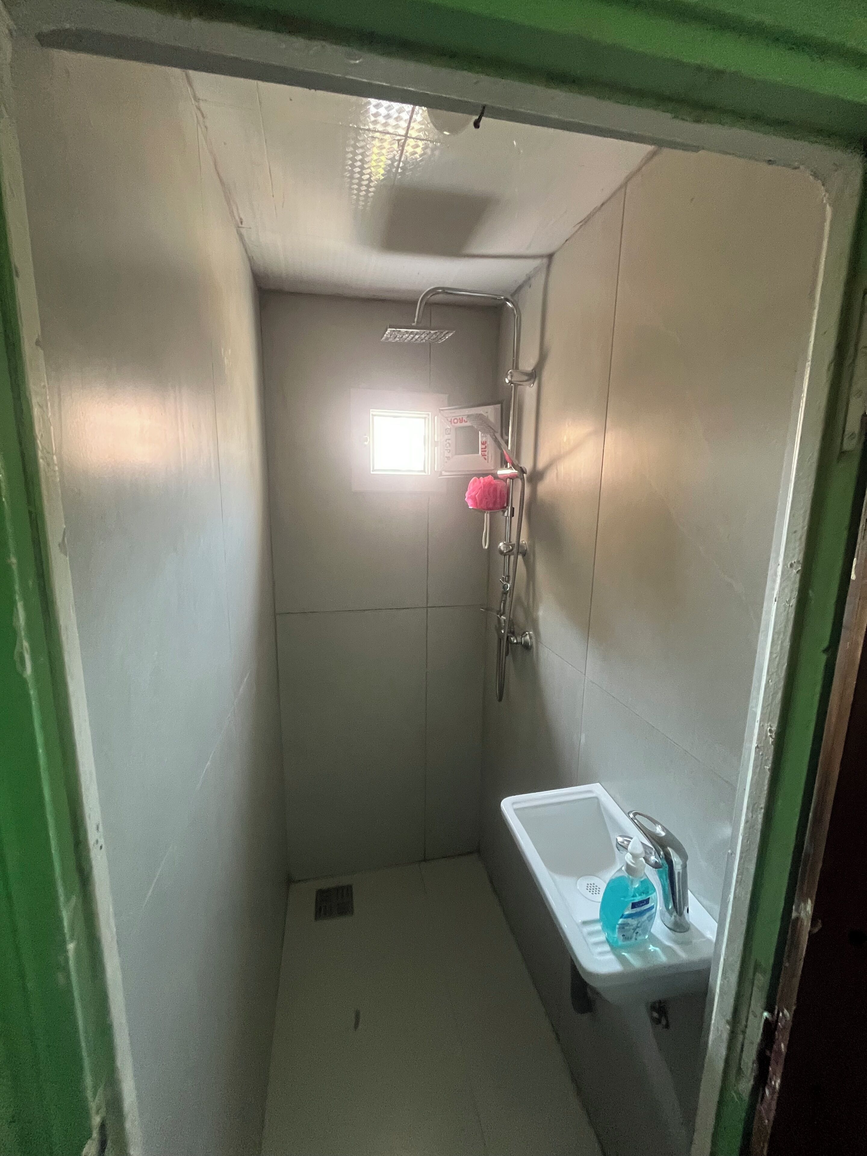 Une petite salle de bain fermée, équipée d’une douche, d’un lavabo et d’une fenêtre.