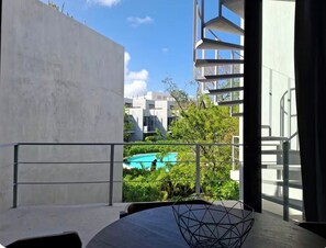 Ein modernes Interieur mit einem geometrischen Metallstuhl, einer Betonwand und Blick auf einen Swimmingpool und Gebäude.