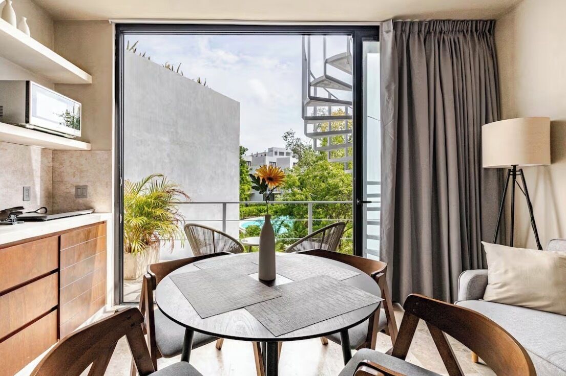Un salón moderno con una mesa redonda, sillas, un sofá, un televisor y vistas a un balcón con plantas y una piscina.