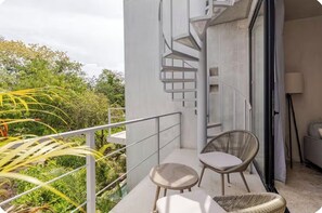 Un balcon agrémenté d’un escalier en colimaçon, de deux fauteuils en osier et d’une petite table.