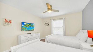 Ein Schlafzimmer mit zwei Betten, einem Deckenventilator, einem Fernseher und motivierenden Wandbildern.