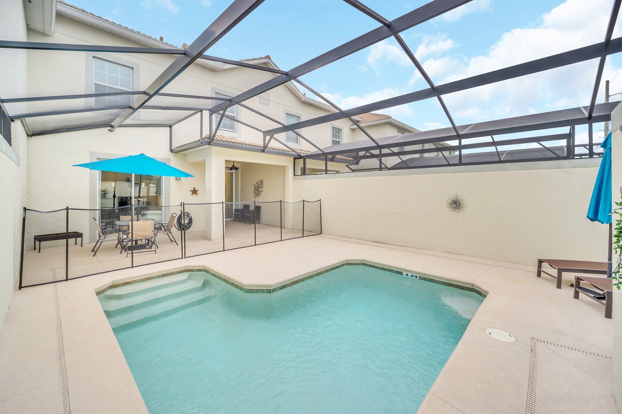 Una piscina con cerramiento de vidrio, una sombrilla azul y un patio con mobiliario.
