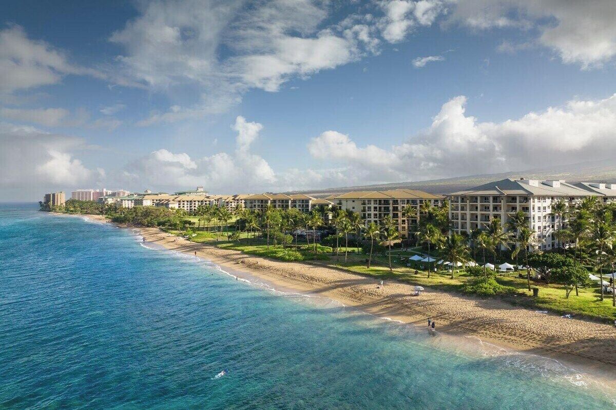 Ein Strandhotel mit mehreren Gebäuden, einem Sandstrand und klarem, blauem Wasser.