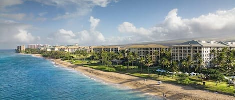A beachfront hotel with multiple buildings, a sandy beach, and clear blue water.