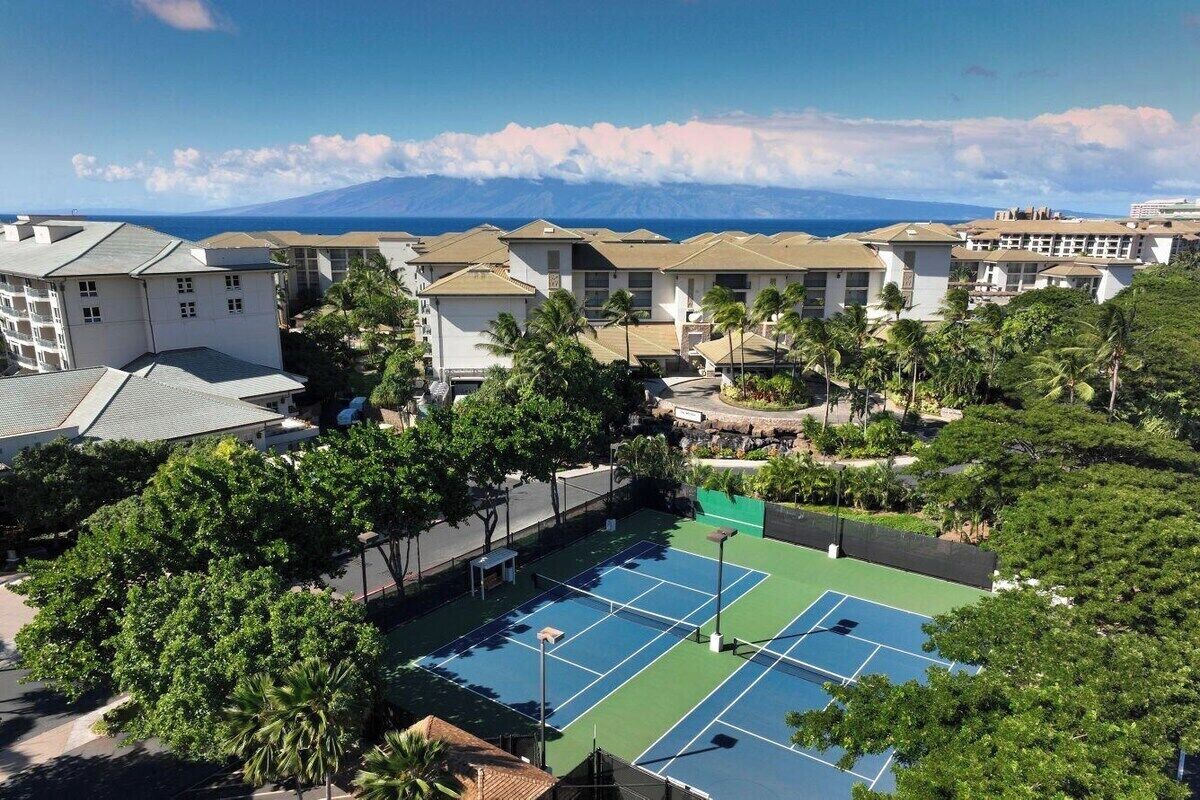 Een woonwijk met meerdere gebouwen, een tennisbaan en uitzicht op de oceaan.