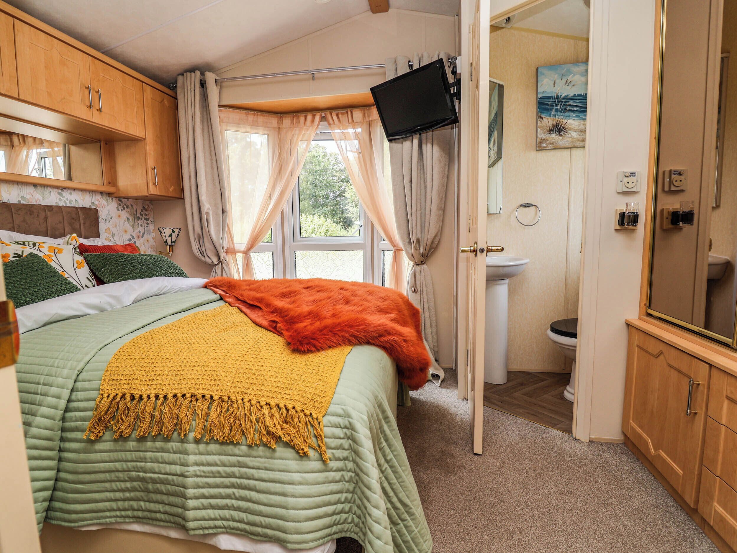 A bedroom with a bed, a television, a bathroom with a sink and toilet, and a window with curtains.