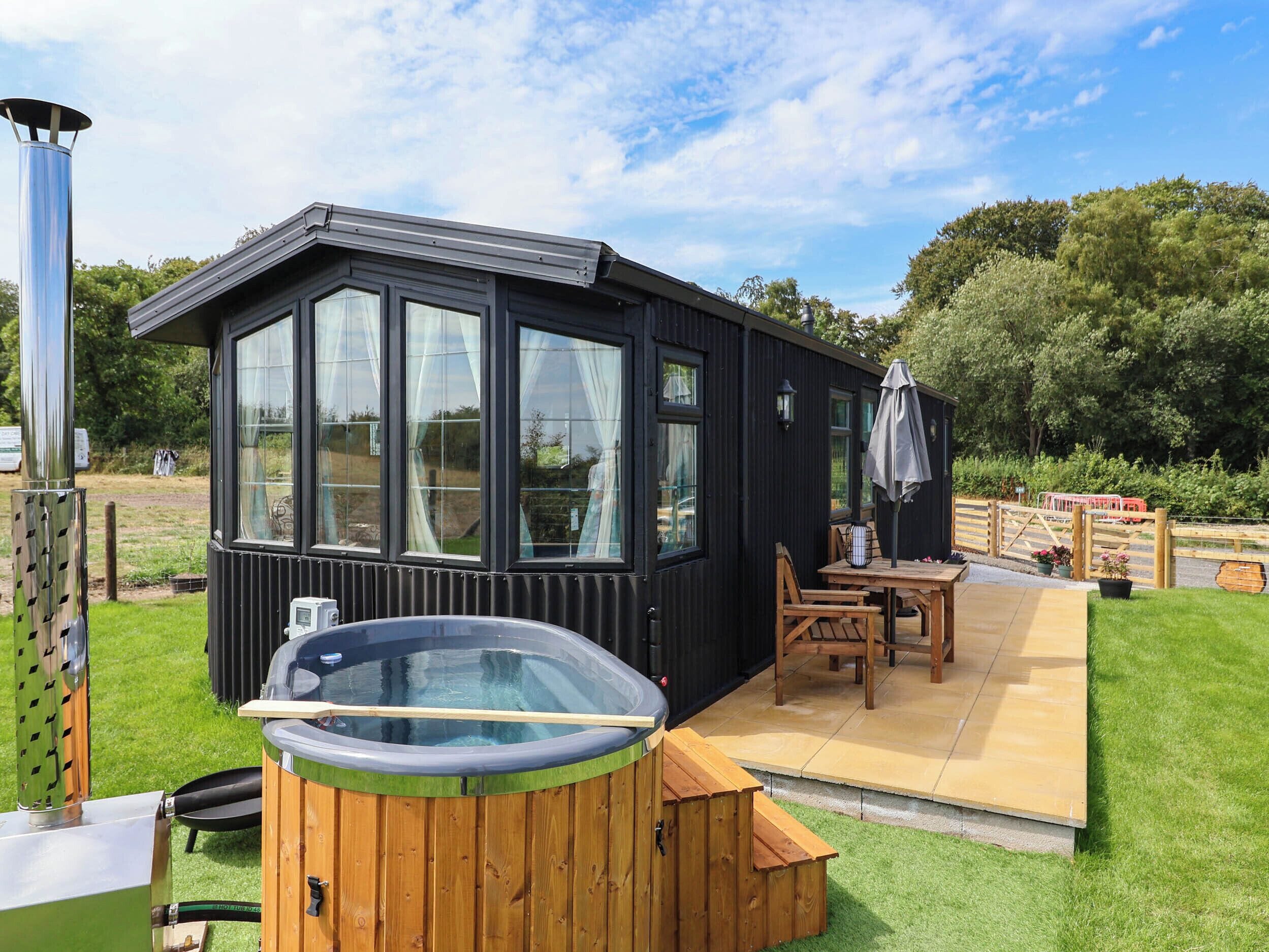 Een zwart metalen gebouw met grote ramen, een hottub en een houten terras.