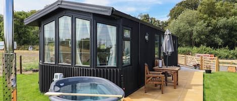 Ein Gebäude aus schwarzem Metall mit großen Fenstern, einem Whirlpool und einer Holzterrasse.