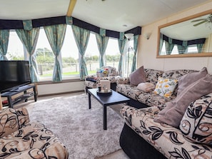 Ein Wohnzimmer mit einer Couch, einem Couchtisch, einem Fernseher und großen Fenstern mit Vorhängen.