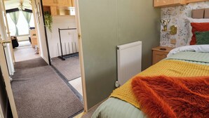 A room with a bed, a radiator, a wooden cabinet, and a door leading to a kitchen area. - Balwen (Mold)