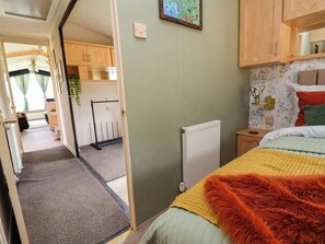 Ein Zimmer mit einem Bett, einem Heizkörper, einem Holzschrank und einer Tür zu einer Küchenzeile.