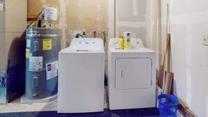 Zona de bugaderia amb dues rentadores, un escalfador d'aigua i productes de neteja.