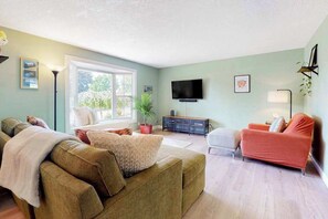 A living room with a sofa, a red armchair, a television, and a large window. - 3BR home with enclosed yard, grill, W&D, fast WiFi (Dundee)