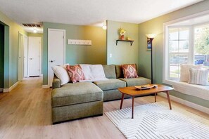 A living room with a sectional sofa, a coffee table, a rug, a floor lamp, and a window with a view.