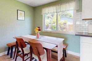 A dining area with a table, chairs, a vase of flowers, and a window with a view of the outdoors.