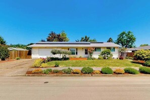 A single-story residential house with a front yard, a driveway, and a wooden fence.