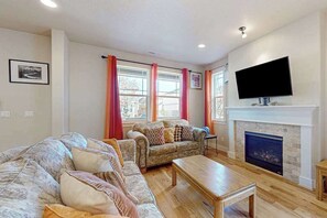 A living room with a sofa set, a fireplace, and a television mounted above it.