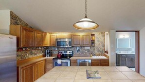 A kitchen with wooden cabinets, a stainless steel refrigerator, a microwave, an oven, and a hanging light fixture.