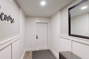 A hallway with a white door, a mirror, and a welcome sign.