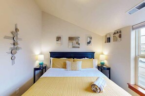 A hotel room with a bed, two bedside tables, wall art, and a window.