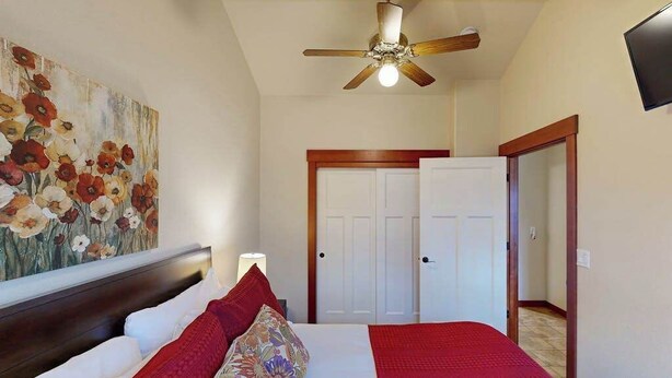 A bedroom with a bed, a ceiling fan, a door, and a wall-mounted TV.