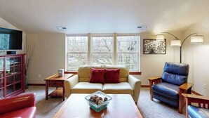 A living room with a sofa, a coffee table, a television, and a window with a view.