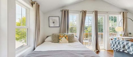 A bedroom with a large bed, a window, curtains, a framed picture, and a balcony.
