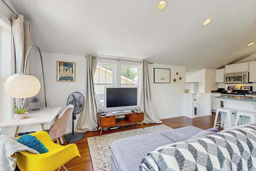 A compact living space with a bed, a desk with a computer, a television, and a kitchenette.