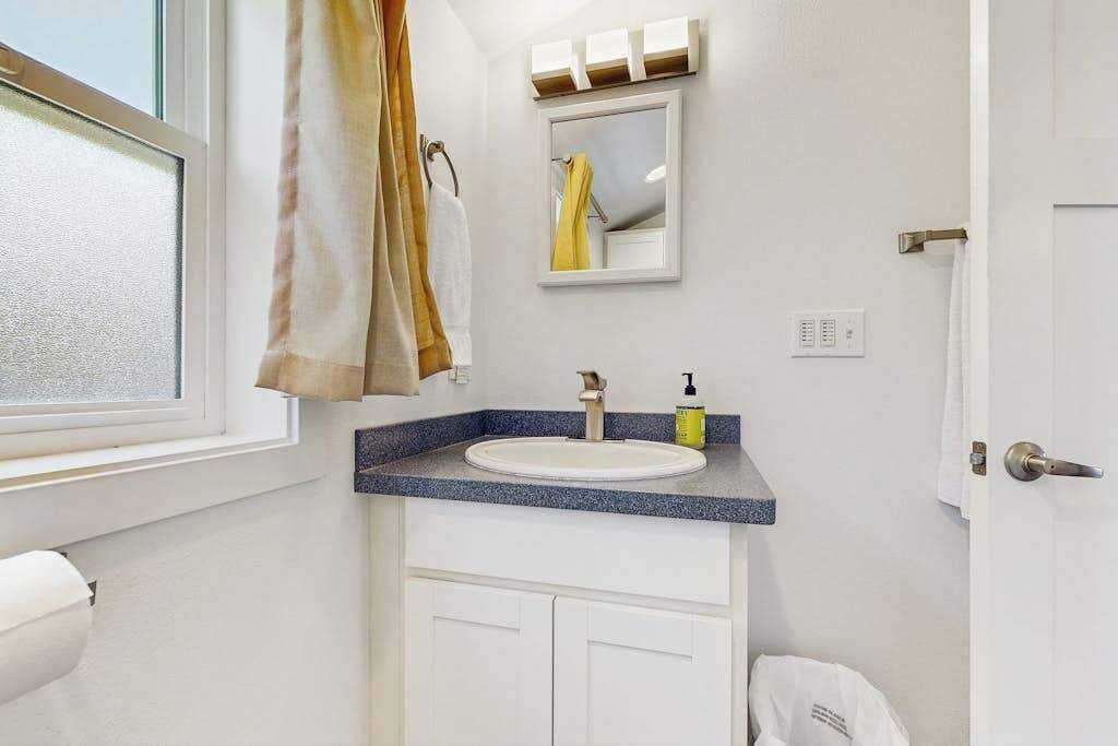 Un baño con un lavamanos blanco, un espejo y una ventana.