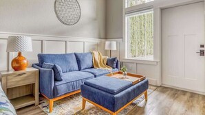 Ein modernes Wohnzimmer mit einem blauen Sofa, passendem Hocker, einem Beistelltisch mit Lampe und einer Wanddekoration.